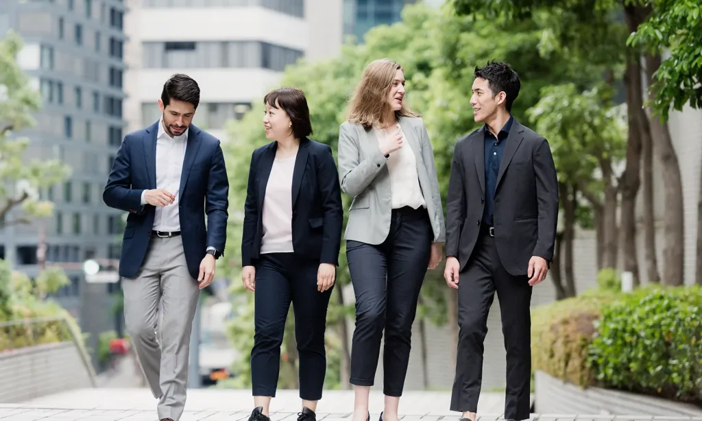 Four diverse business students in professional attire walking and conversing outdoors on a city campus.