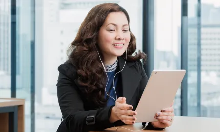 A woman wearing a headset and using a tablet for an online event in a modern office lounge.