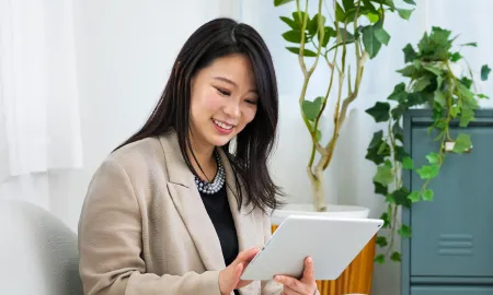 A business school student smiling while participating in an online session on a tablet.