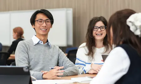 Business school students smiling and chatting together at a desk during a study session.