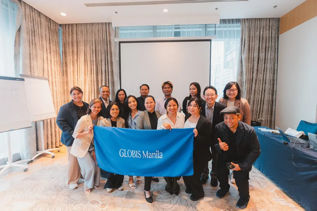 A group of business school students and faculty pose in a conference room holding a blue banner reading GLOBIS Manila.