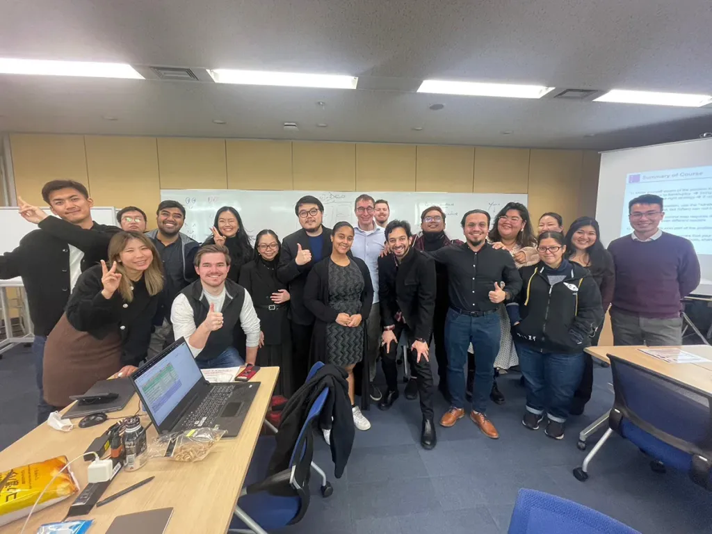 A large group of diverse business school students and faculty smiling and posing together in a classroom.