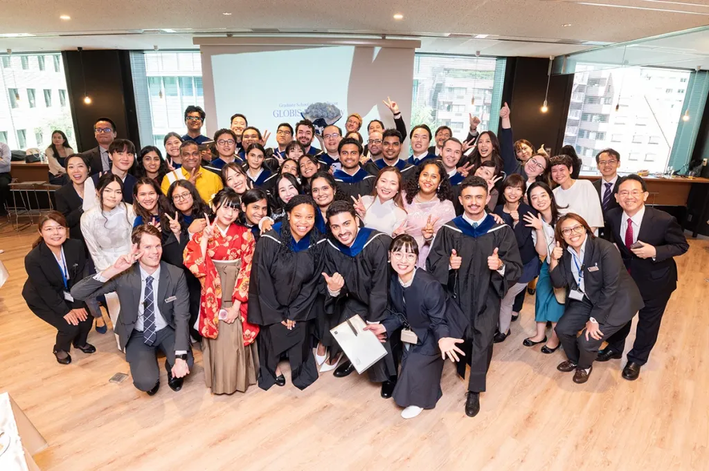 A large group of diverse business school students in graduation gowns, smiling and posing at a graduation event.