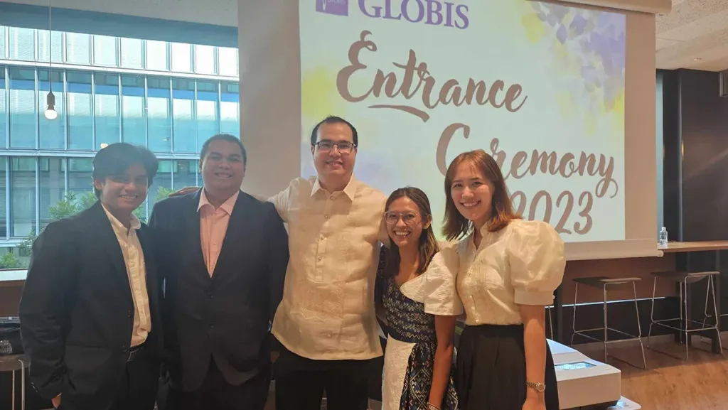 Five people posing at a business school event in front of a screen reading "GLOBIS Entrance Ceremony 2023".