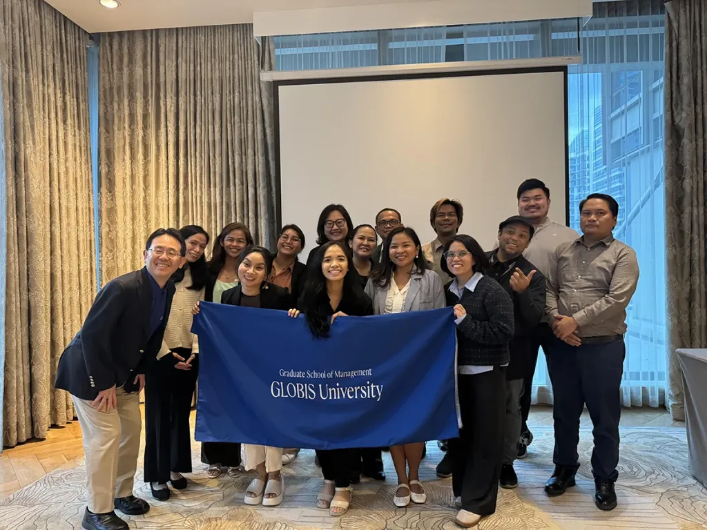Business school students and faculty posing with a blue banner reading "Graduate School of Management GLOBIS University".