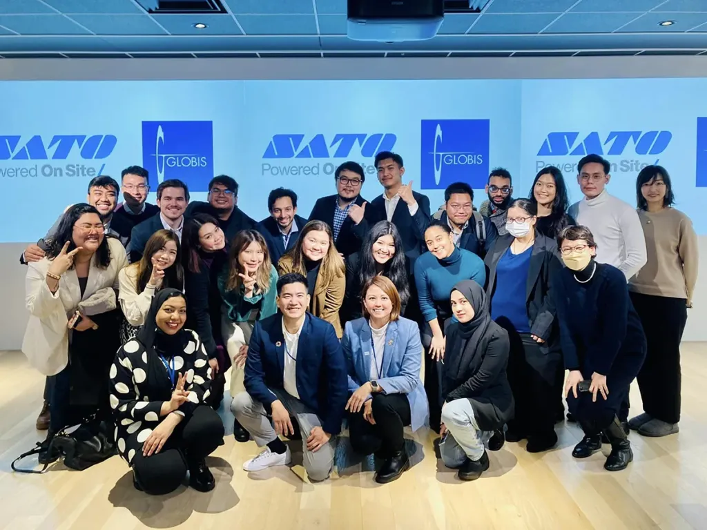 A large group of diverse business school students and faculty smiling and posing together in a classroom.