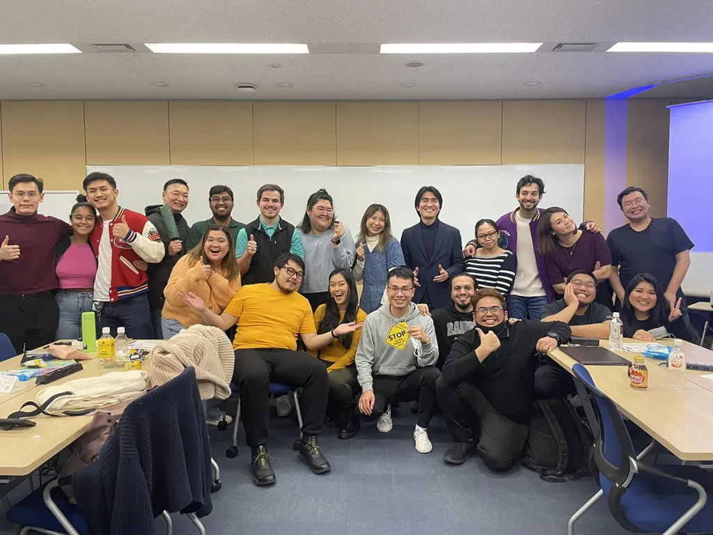 A large group of business school students posing in front of a screen displaying SATO Powered On Site and GLOBIS logos.
