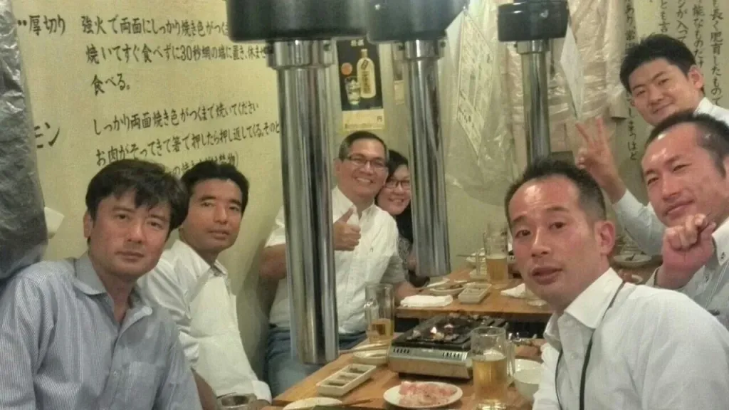 Seven business school students smiling and posing together around a table at a Japanese BBQ restaurant.