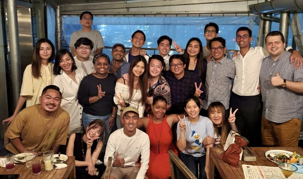 A large group of diverse business school students smiling and posing together during a social gathering at a restaurant.