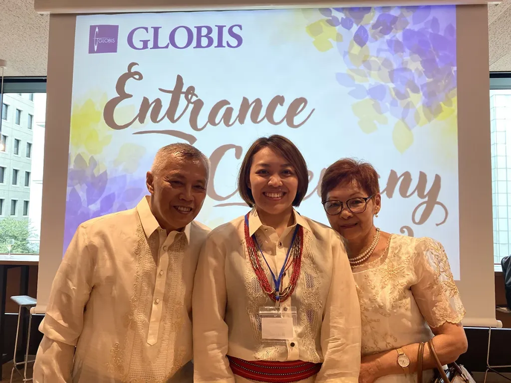 A student and her parents in traditional attire posing before a GLOBIS Entrance Ceremony screen.